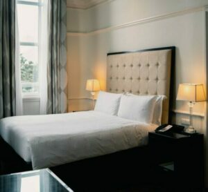 Photo by Albert Vincent. A double bed in a hotel room with a window and lights. 